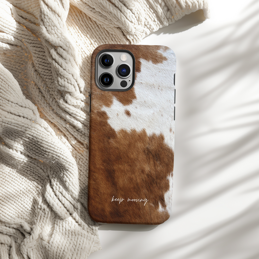 Phone case with cow print design and 'keep moving' text on a textured surface