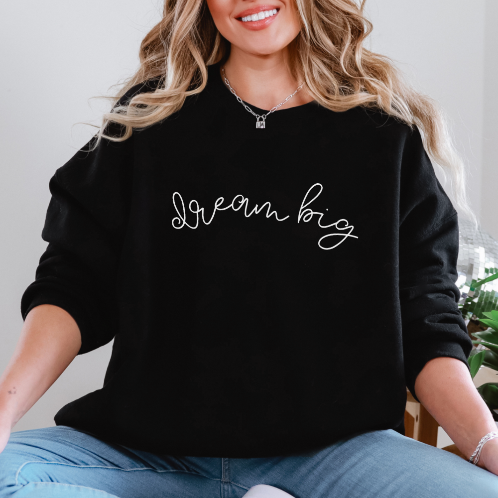 Person wearing a black sweatshirt with 'Dream big' text, sitting indoors.