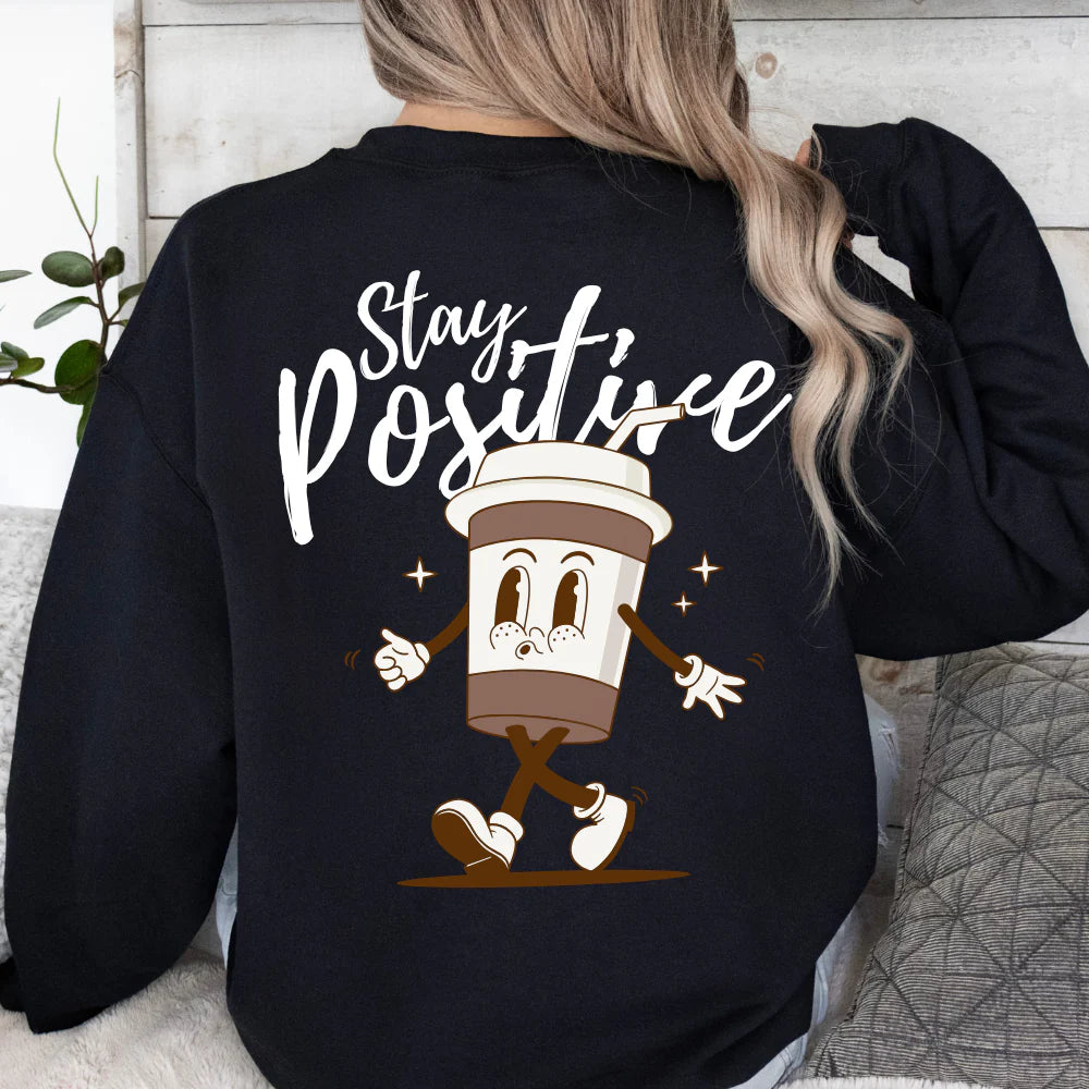 Person wearing a black sweatshirt with a cartoon coffee cup and 'Stay Positive' text on the back.