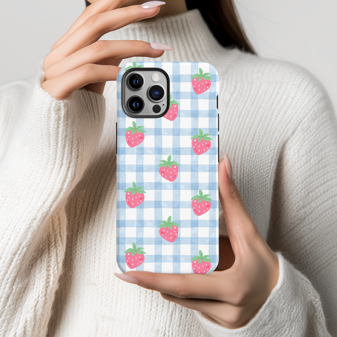 Phone case with strawberry pattern held by a person wearing a white sweater