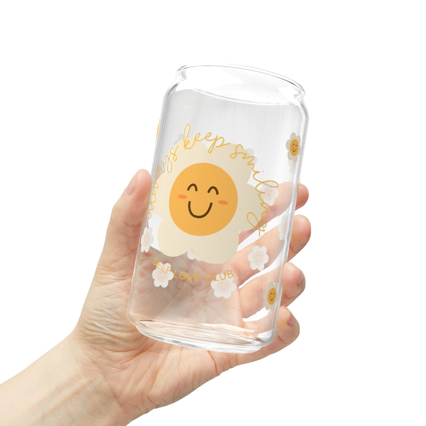 Clear glass tumbler with a happy flower design held by a hand on a white background