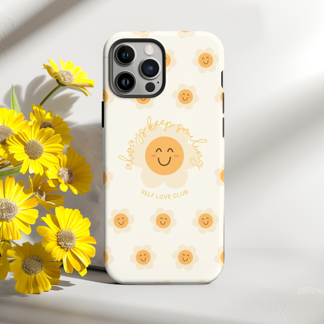 Phone case with happy face design and text, surrounded by yellow flowers on a light background