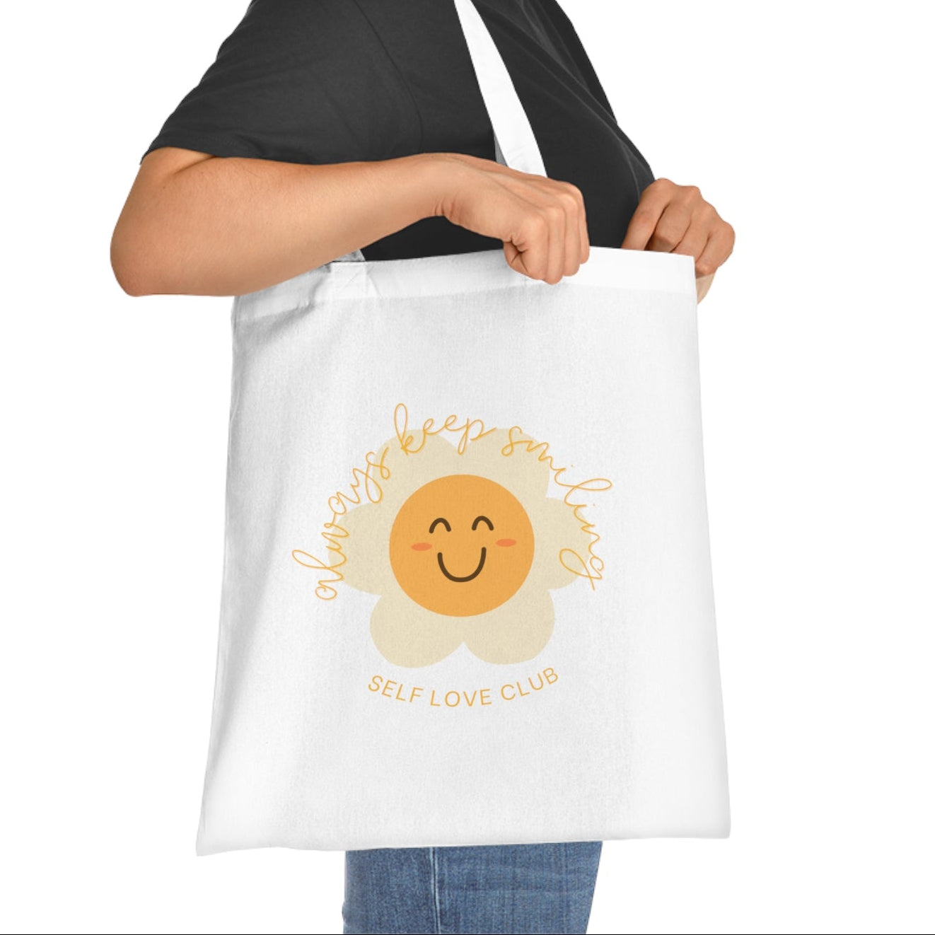 Woman holding a tote bag with a happy flower design and 'Self Love Club' text on a white background