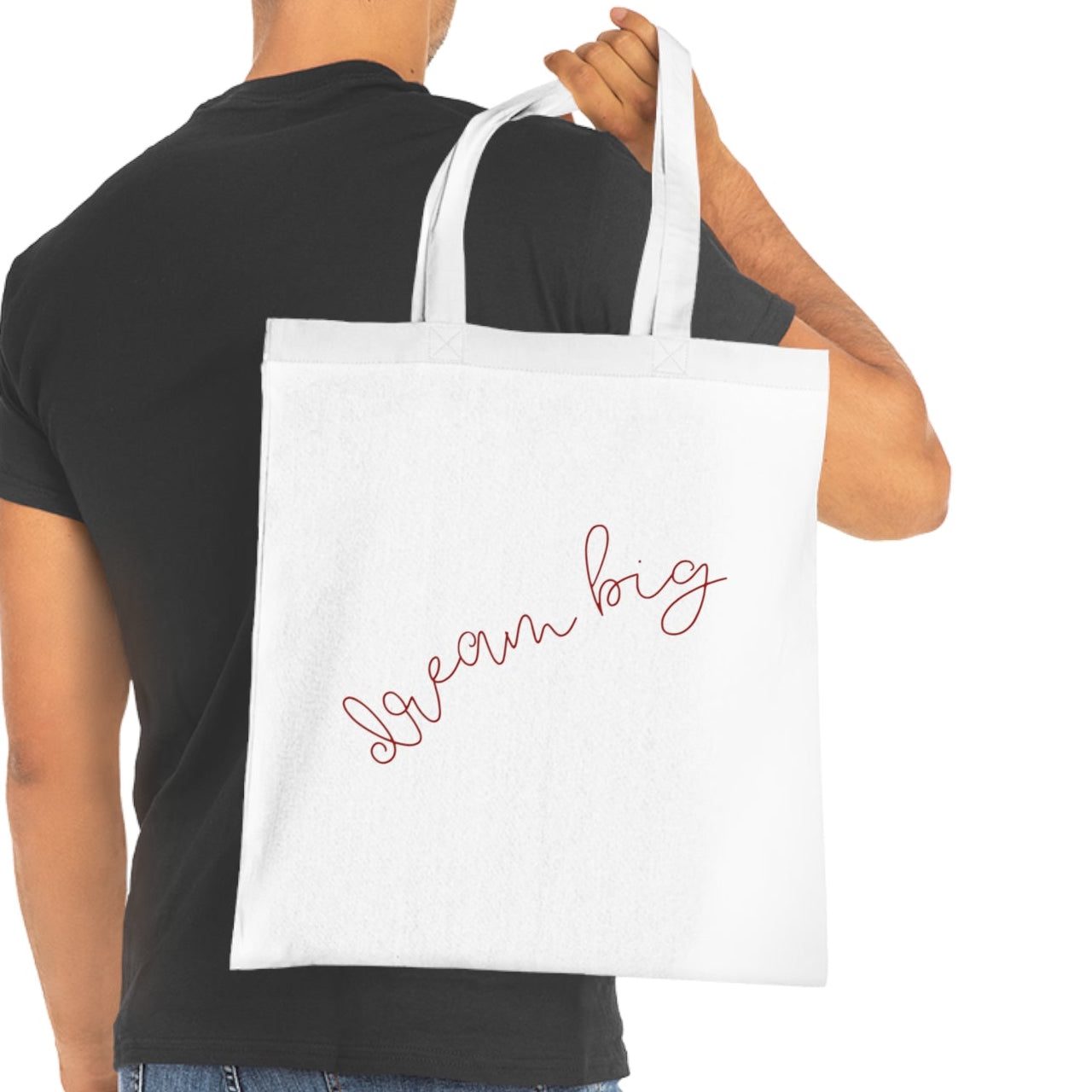 Man holding a white tote bag with 'Dream Big' text on a white background