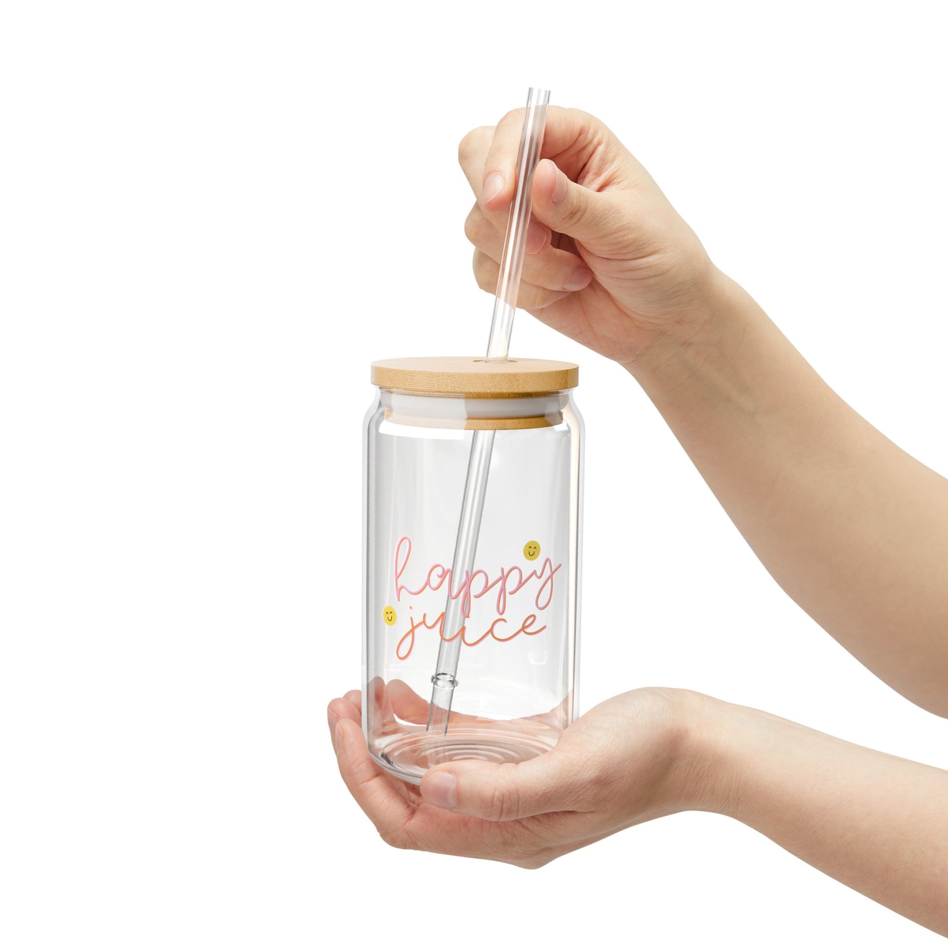 Glass tumbler with wooden lid and straw held by a hand on a white background