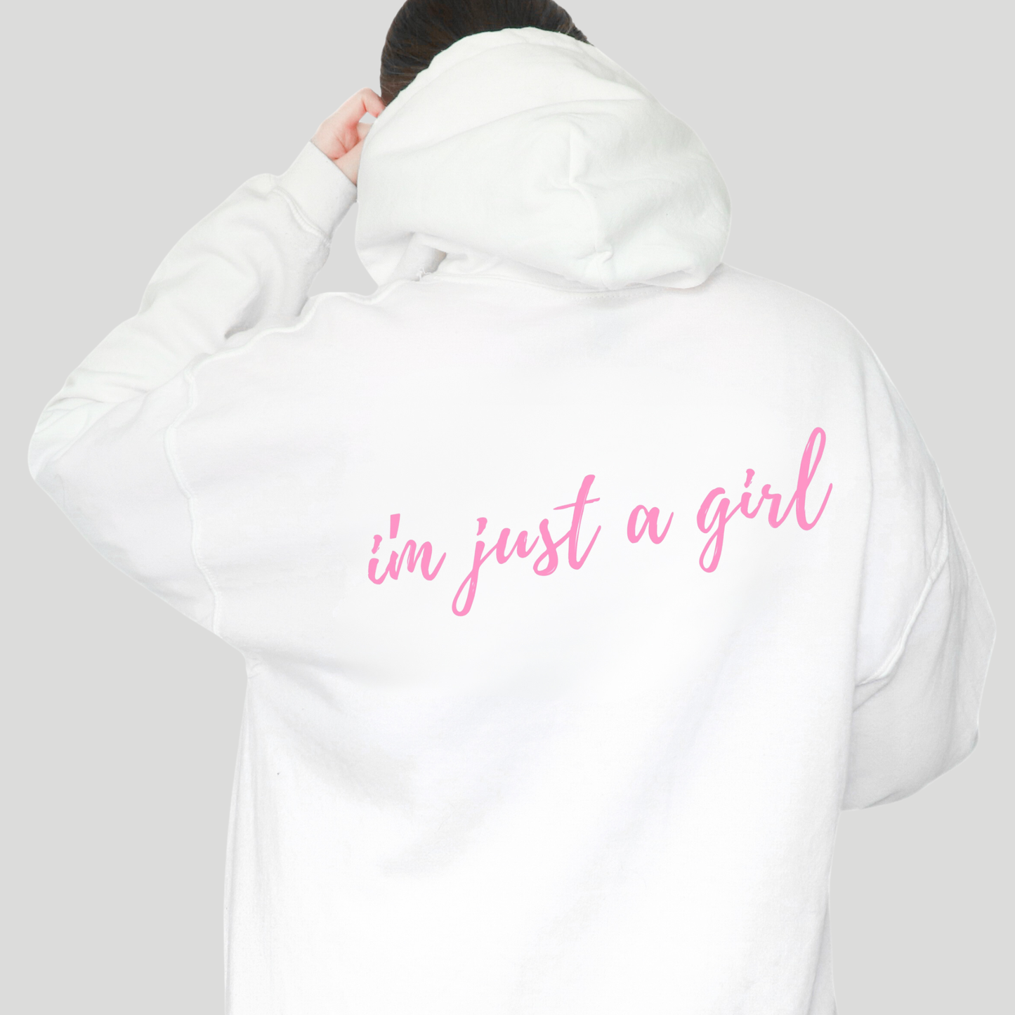White hoodie with 'i'm just a girl' text in pink on the back, worn by a person against a plain background.