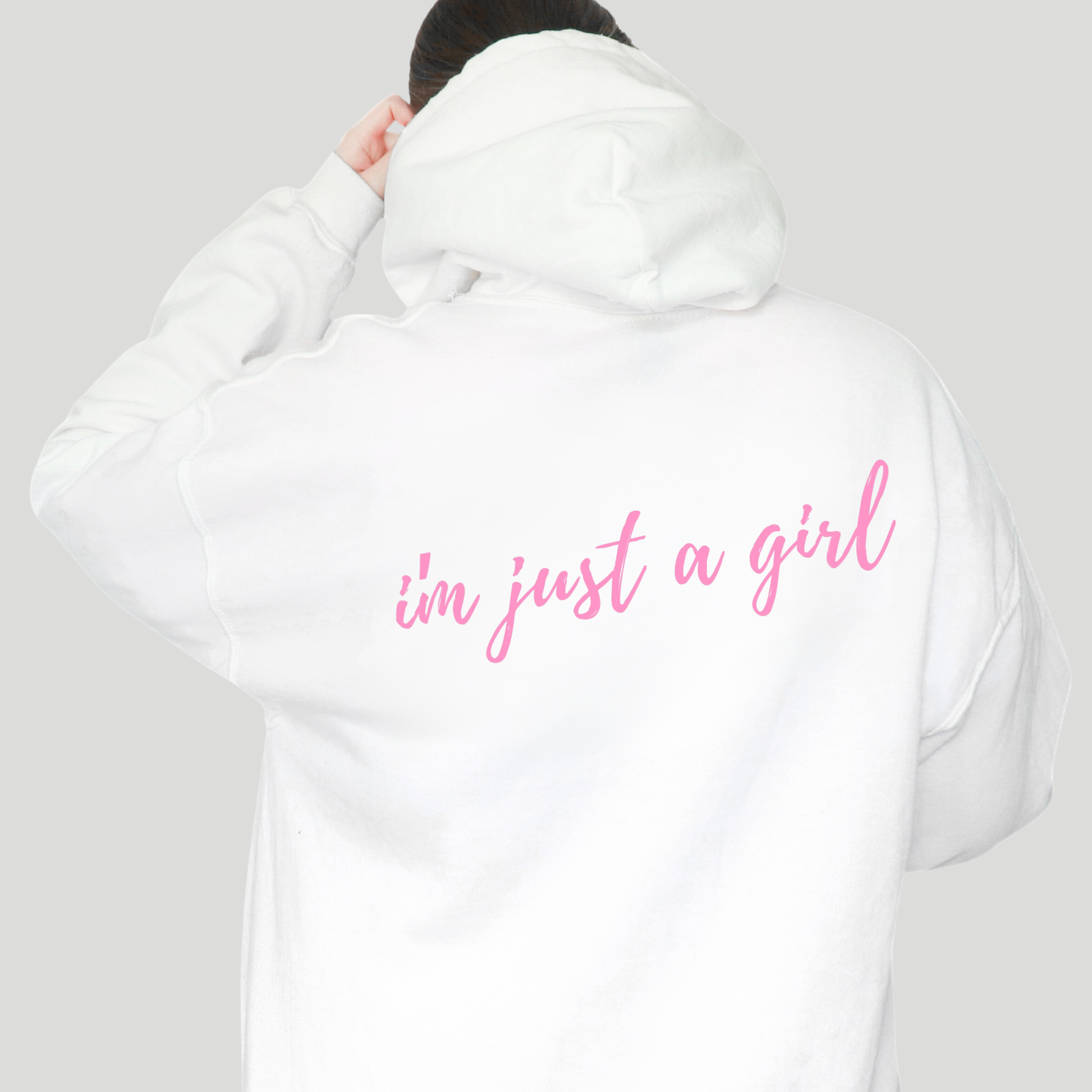 White hoodie with 'i'm just a girl' text in pink on the back, worn by a person against a plain background.