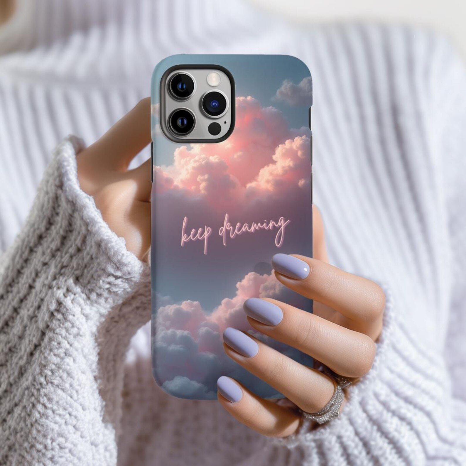 Phone case with cloud design and 'keep dreaming' text held by a person wearing a white sweater.