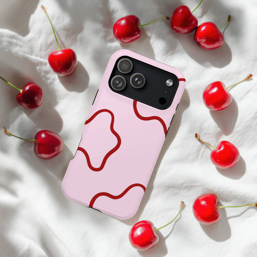 Pink phone case with red design on a white surface with cherries