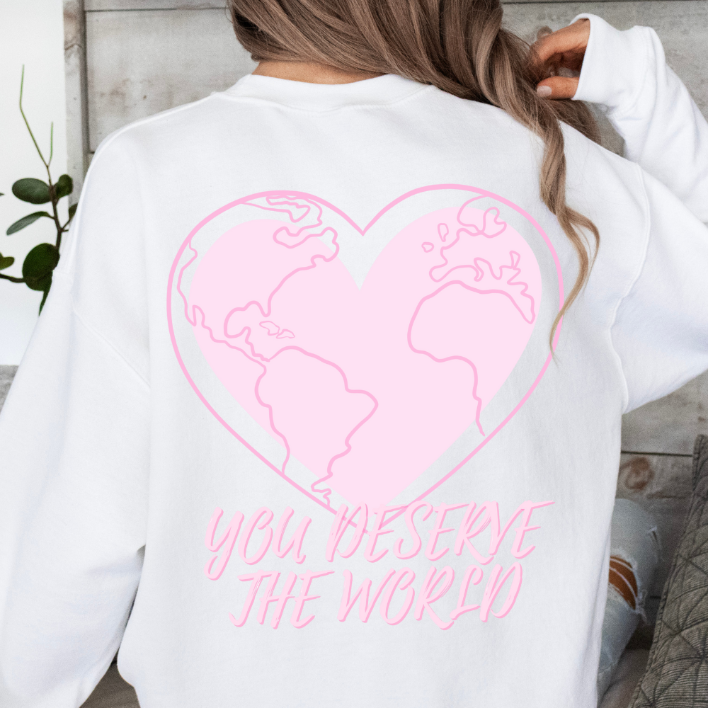 White sweatshirt with pink heart and world map design on the back, worn by a person.